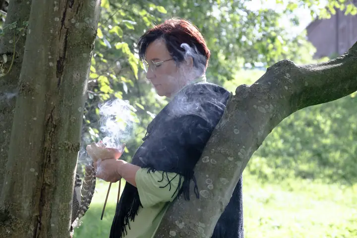 Nicole Dreis hält eine rauchende Räucherschale am Baum
