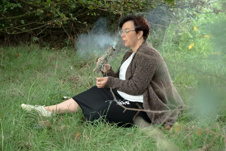 Nicole Dreis sitzt im Gras und pustet in ein rauchendes Räucherbündel