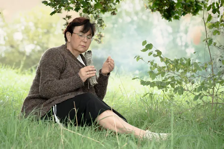 Nicole Dreis sitzt mit einem Räucherbündel auf der Wiese