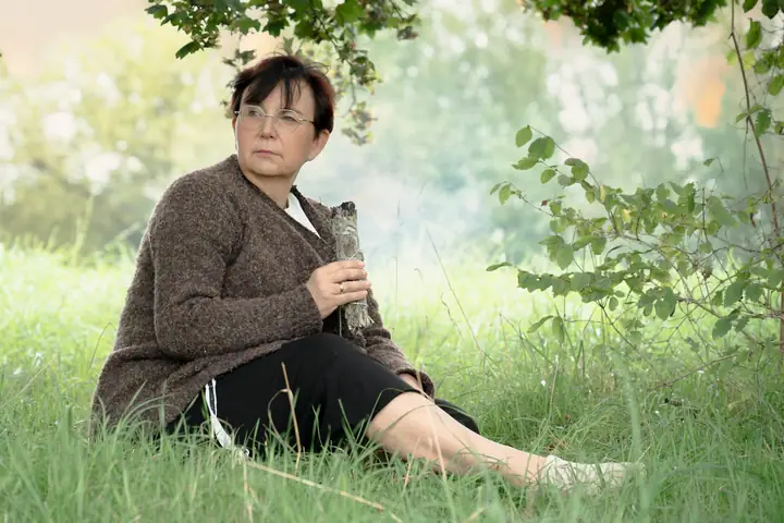 Nicole Dreis sitzt ruhig im Gras, das Räucherbündel in der Hand