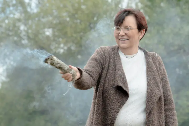 Nicole Dreis streckt lachend ein rauchendes Räucherbündel aus