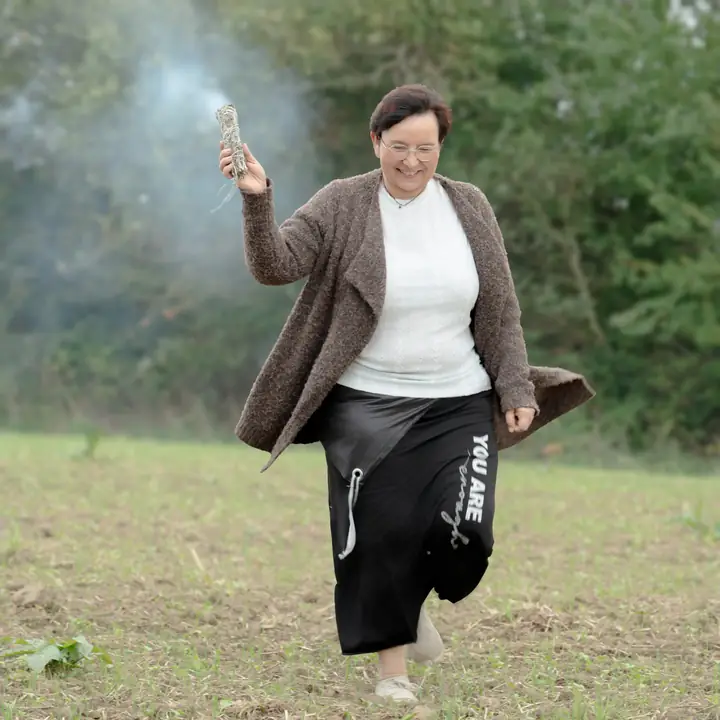 Nicole Dreis tanzt mit einem rauchenden Räucherbündel über das Feld
