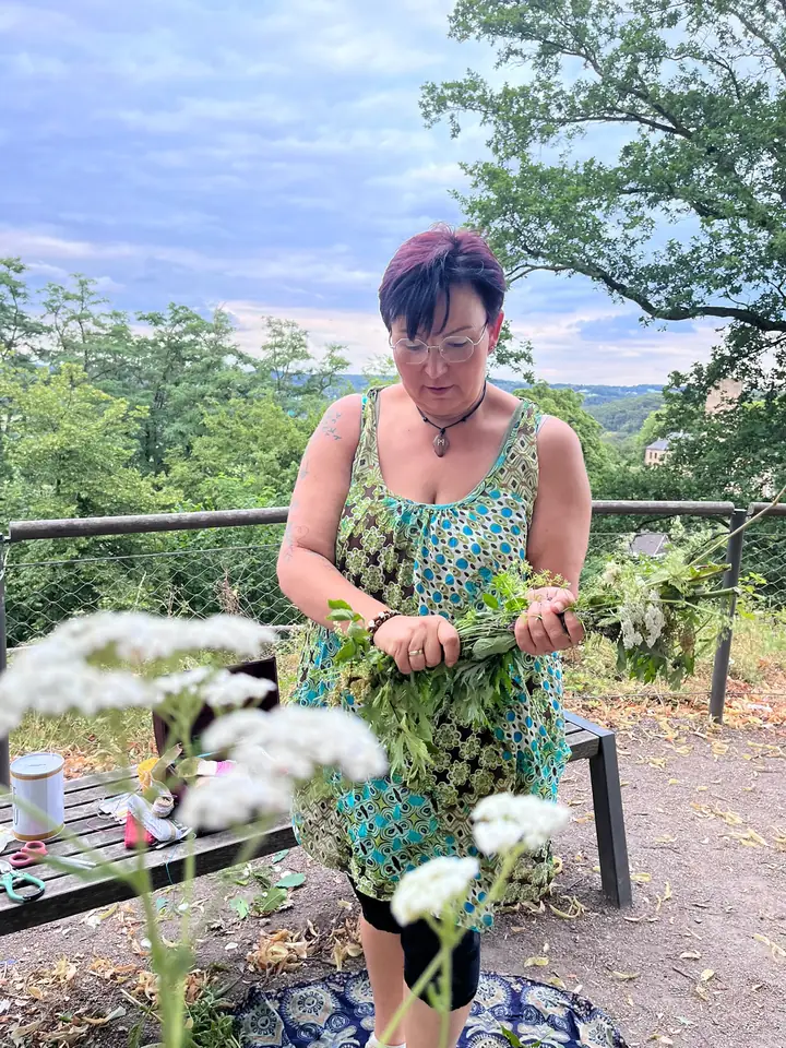 Nicole Dreis bindet Kräuter, im Vordergrund blühende Wildblumen