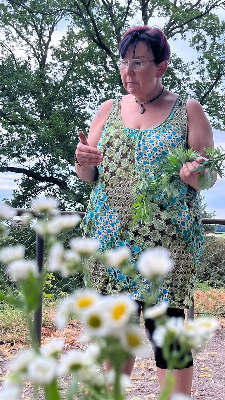 Nicole Dreis erzählt draußen über Kräuter, vor ihr blühen Wildblumen